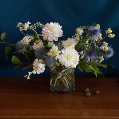 a glass vase filled with white and blue flowers on top of a wooden table next to nuts