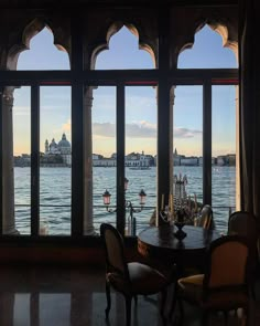 a dining room with large windows overlooking the water and buildings in the distance at sunset