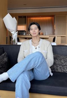 a woman sitting on top of a black couch next to a white vase with flowers in it