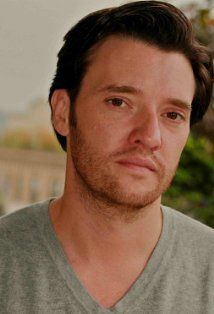 a close up of a person wearing a gray shirt and looking at the camera with a serious look on his face