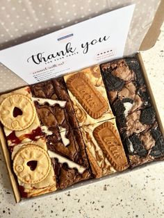 a box filled with lots of different desserts on top of a counter next to a thank you sign