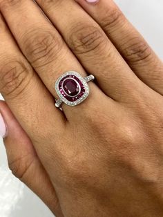 a woman's hand holding a ring with a red stone in the middle and white diamonds around it