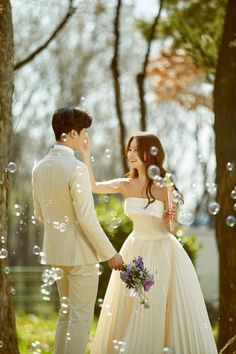 a bride and groom standing next to each other in front of trees with soap bubbles