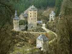 an old castle sits on top of a hill surrounded by trees and bushes in the woods