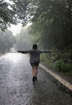 a person walking in the rain with their arms spread out and holding an umbrella over their head