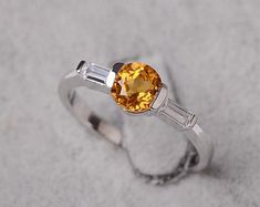 a ring with an orange and white stone in the center, sitting on top of sand