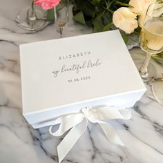 a white box with a name on it sitting next to some wine glasses and flowers