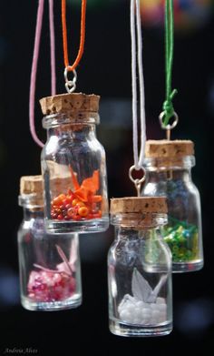 three glass jars filled with different types of small objects hanging from strings on a black background