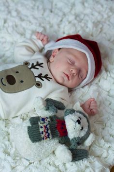 a baby is laying down next to a stuffed animal and wearing a santa claus hat