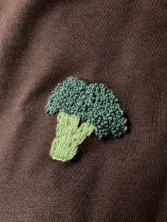 a broccoli embroidered onto a brown sweater with green leaves on the front and bottom