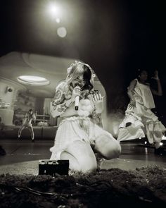 a woman sitting on the ground holding a microphone in her hand and singing into a microphone