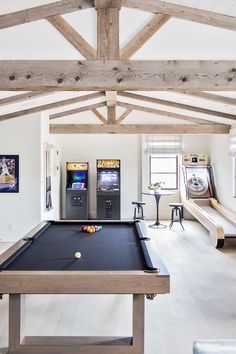 a pool table and arcade machines in a room with white walls, wood beams and flooring