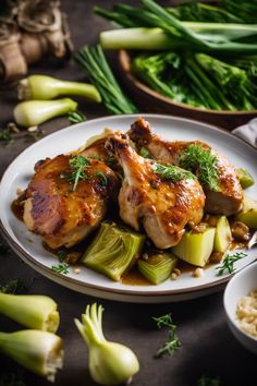 some chicken and vegetables on a white plate with gravy in the middle next to green onions