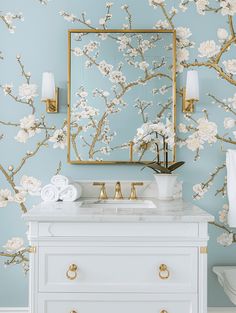 a bathroom with blue and white wallpaper, gold framed mirror, marble counter top sink and golden faucet