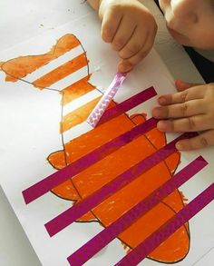 a young boy is making a paper cut out of the shape of an orange fish