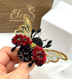 a hand holding a brooch with flowers and a bee on it's back