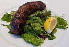 a sausage and salad on a plate with lemon wedges in the middle, ready to be eaten