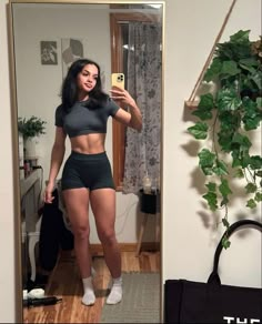 a woman taking a selfie in front of a mirror wearing black shorts and grey shirt