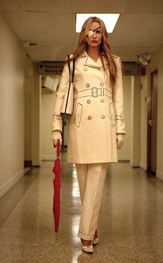 a woman walking down a hallway with an umbrella in her hand and wearing a trench coat