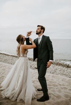 a man and woman standing on top of a beach next to the ocean drinking from bottles