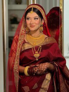 a woman in a red and gold bridal outfit with jewelry on her head, standing next to a mirror