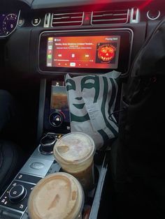 two cups of coffee sitting on top of a car dashboard next to a paper bag