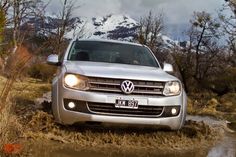 a silver vw passanger driving through mud in front of snow capped mountain range