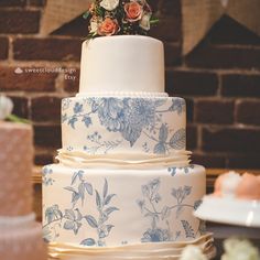 a three tiered wedding cake with blue and white flowers on it's side