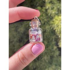 a hand holding a tiny glass bottle with pink and purple things in it's mouth