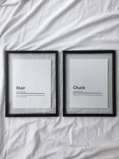 two black framed pictures sitting on top of a white sheet