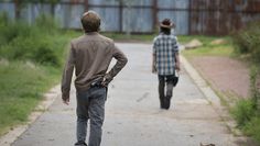 two young men walking down a path in the grass with their backs to each other