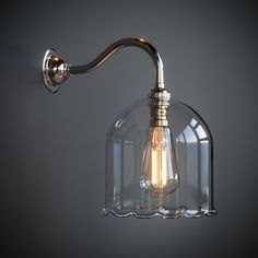 a light that is on the wall next to a glass lamp shade and metal arm