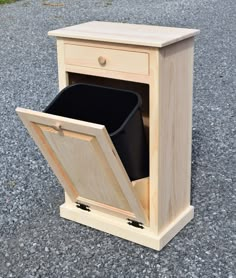 a wooden cabinet with a black trash can in the bottom drawer and one door open