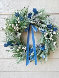 a wreath hanging on the side of a building with blue ribbon and white flowers in it