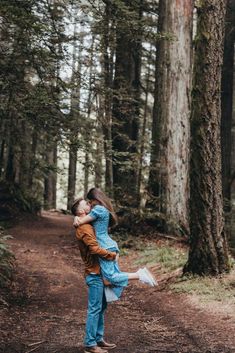 a man holding a woman in the middle of a forest with lots of tall trees