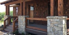 a wooden porch with stone pillars and railings next to a building that has wood shingles on it