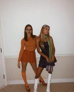 two young women standing next to each other in front of a white wall wearing short skirts and knee high boots