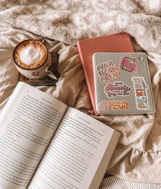 an open book sitting on top of a bed next to a cup of hot chocolate