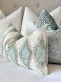 two pillows sitting on top of a white bed covered in blue and green fabrics