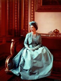 an old photo of a woman in a blue dress sitting on a chair with a painting behind her