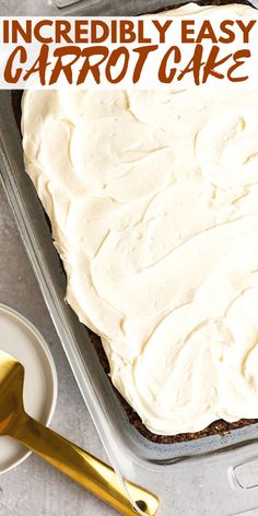 a cake with white frosting in a pan on top of a table next to a gold spoon