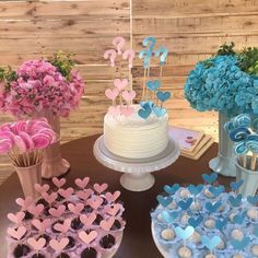 a table topped with cakes and cupcakes covered in blue icing next to vases filled with flowers