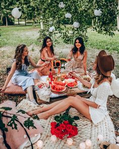 four women sitting around a picnic table with food on it