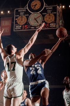 two basketball players jump for the ball in front of three other players and an analog clock hangs above them