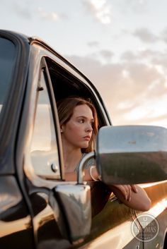 a woman sitting in the drivers seat of a car with her reflection in the side mirror