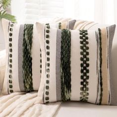 two decorative pillows on a couch in front of a window with white and green curtains