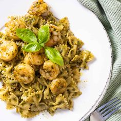 pasta with shrimp and pesto sauce on a white plate next to a silver fork