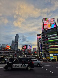 a taxi cab driving down a street next to tall buildings with billboards on them