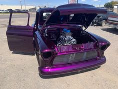 an old purple car with its hood up and engine in the back seat, parked on concrete