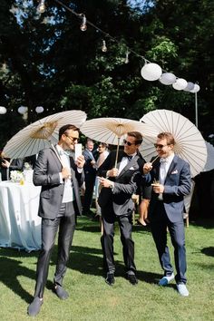 two men in suits are holding umbrellas at an outdoor wedding reception on the grass